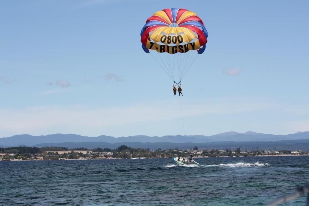 A parasail with '0800 BIG SKY' text over a body of water with a distant shoreline and mountains.