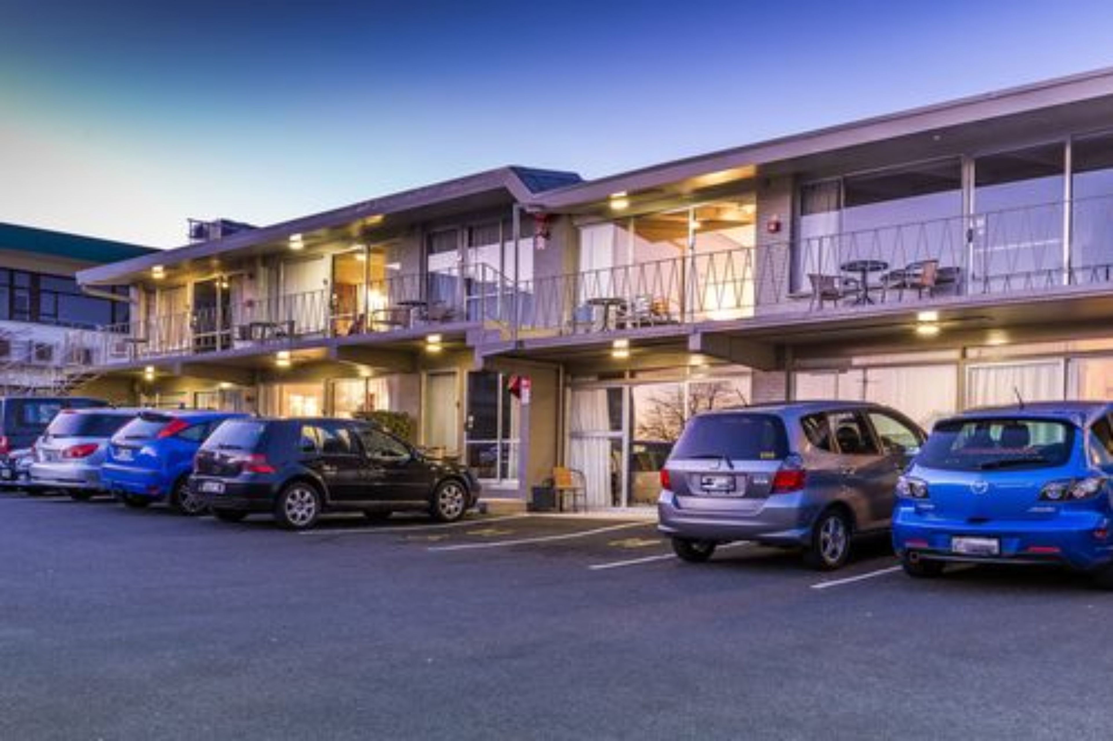 A motel with multiple floors, outdoor seating, and a parking lot with several cars.