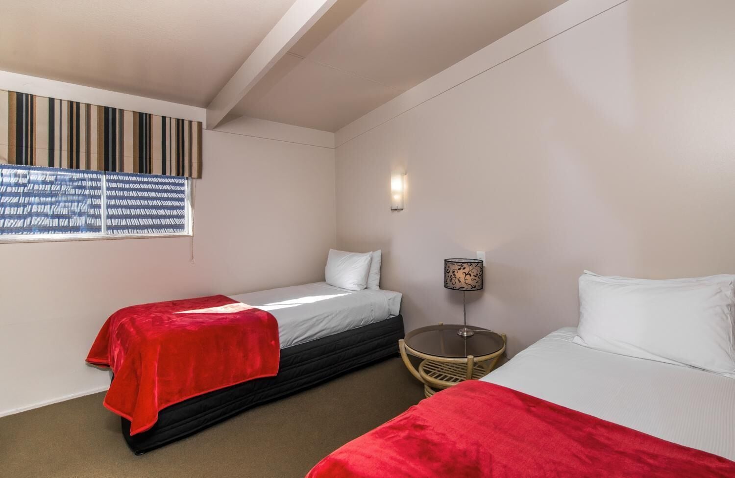 Una camera d'albergo con due letti, un tavolino rotondo e una finestra con tende a righe.