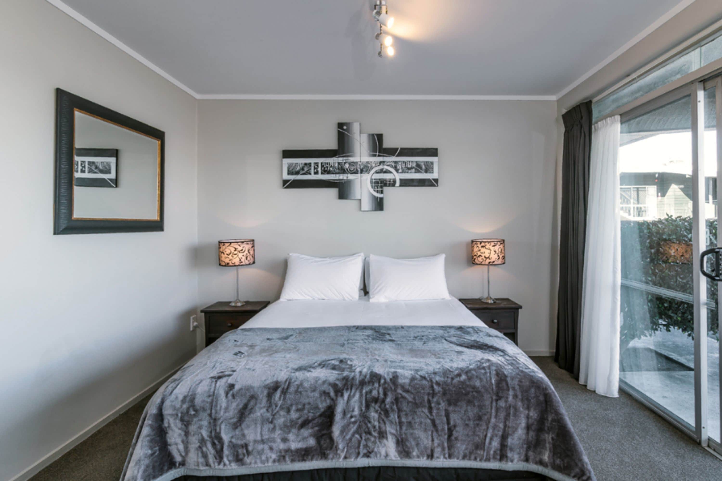 A modern hotel room with a large bed, two bedside lamps, a wall-mounted artwork, and a large window with curtains.
