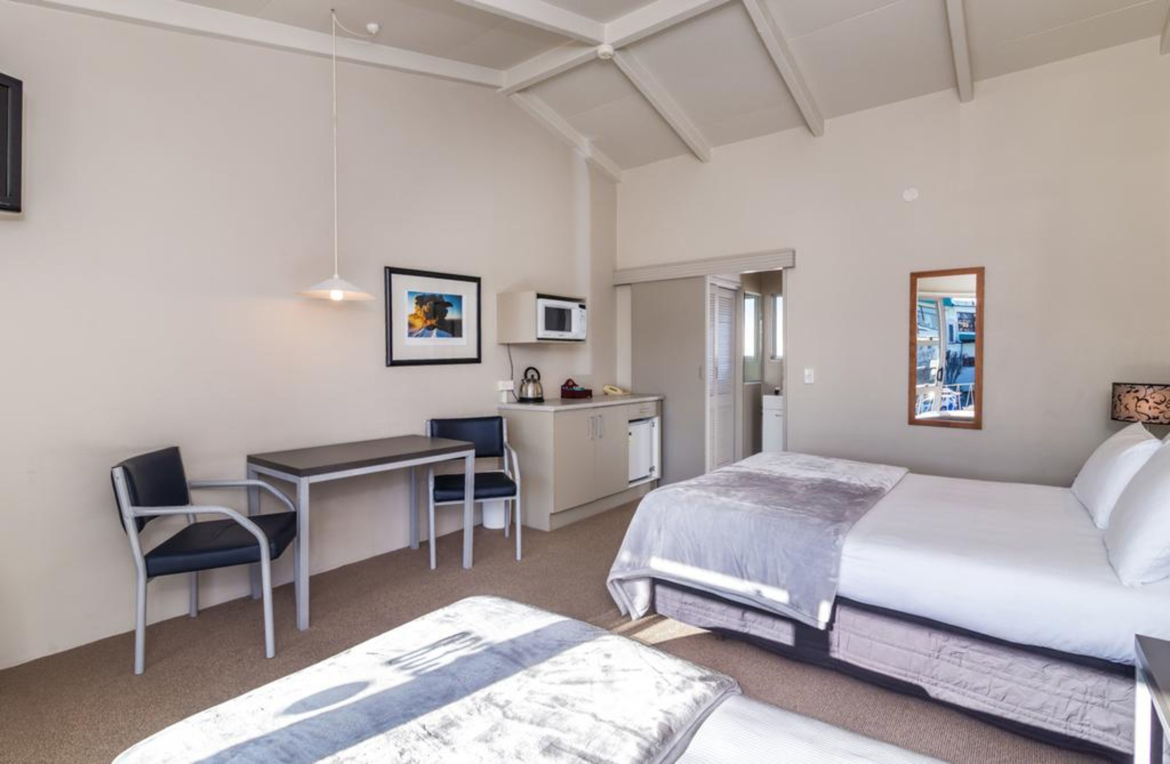 A hotel room with a bed, two chairs, a desk, a microwave, and a small kitchenette.