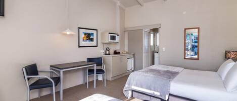 A hotel room with a bed, two chairs, a desk, a microwave, and a small kitchenette.
