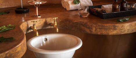 A bathroom with a white basin, copper faucets, a round mirror, and toiletries on a tray.