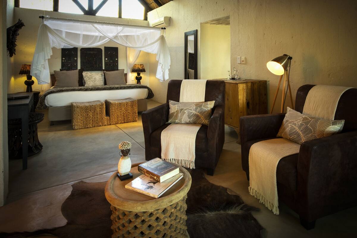 A cozy room with a bed, two armchairs, a small table with books, and a lamp.