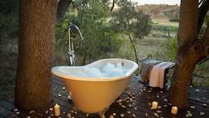A bathtub filled with bubbles, surrounded by trees, on a wooden deck with candles and flower petals. - Pondoro Game Lodge  - Open to Kruger Park (Hoedspruit)