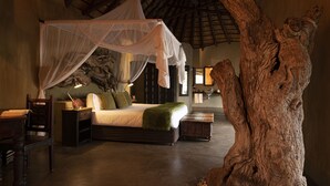 A bedroom with a canopy bed, a large tree sculpture, and a rustic decor style. - Pondoro Game Lodge  - Open to Kruger Park (Hoedspruit)