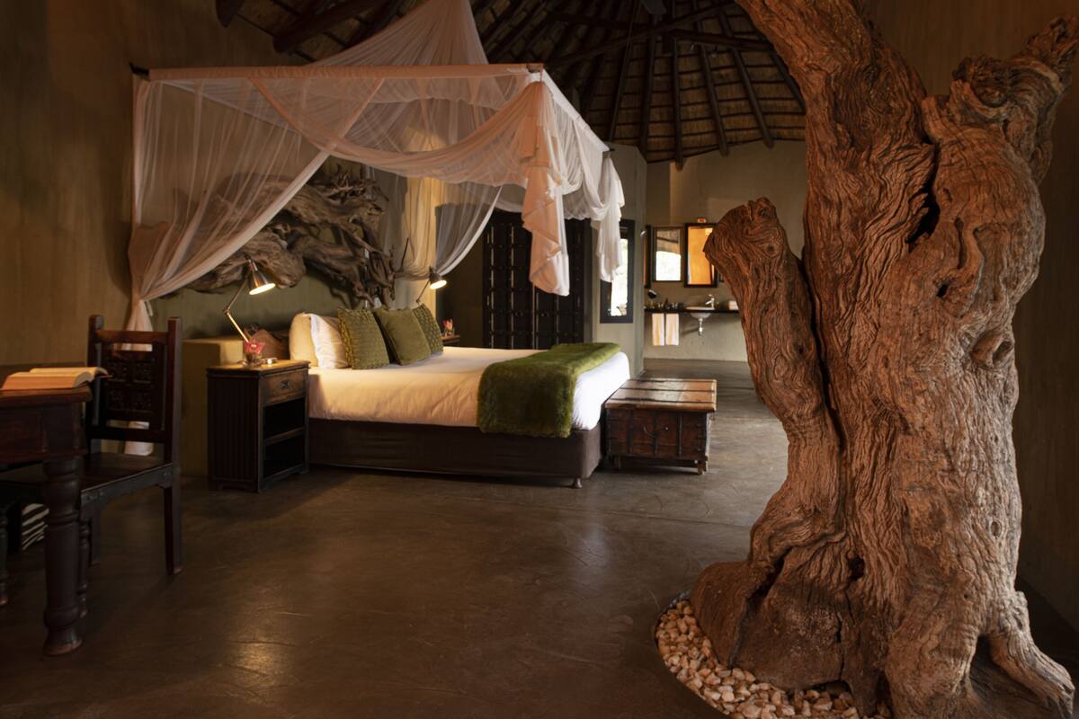 A bedroom with a canopy bed, a large tree sculpture, and a rustic decor style.
