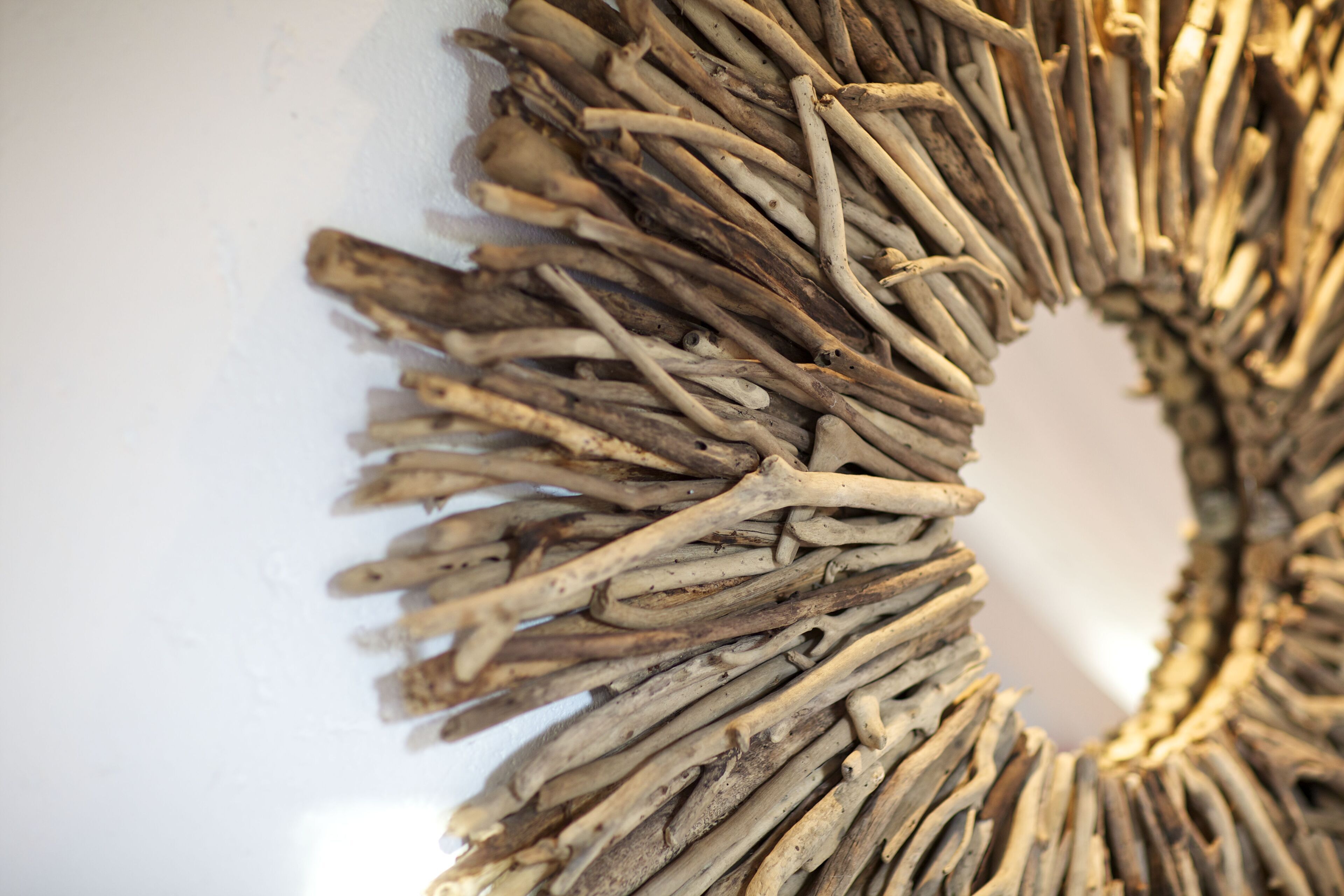 Primer plano de una pared con un arreglo circular de materiales naturales, posiblemente ramas o madera a la deriva, creando un diseño texturizado.