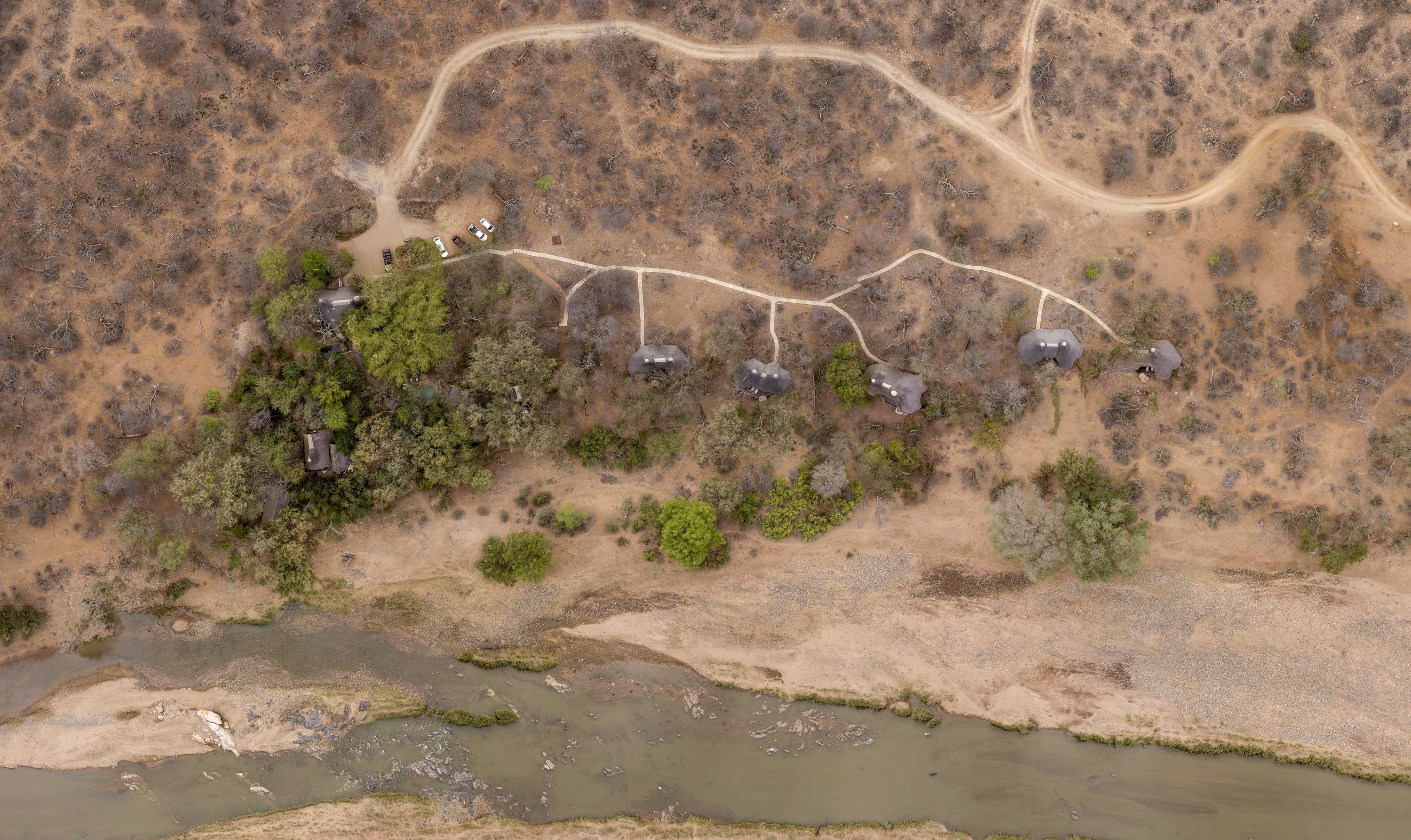 An aerial view of a remote area with a dirt road, several vehicles, and a small body of water.