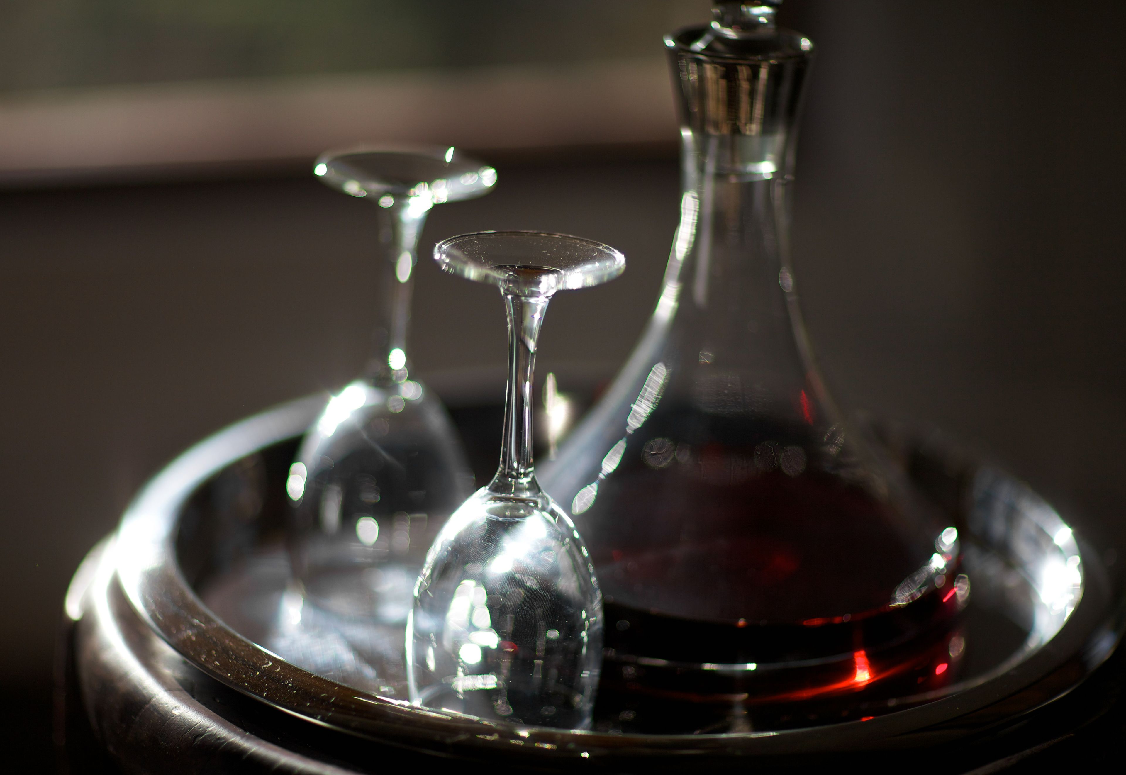 A close-up of a glass decanter and two wine glasses on a reflective tray.