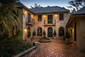 A two-story building with a courtyard, featuring a fountain, potted plants, and a brick pathway.