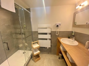 A modern bathroom with a glass shower enclosure, a wooden vanity with a sink, and a towel rack. - Hotel Les Ancolies (Beaufort)