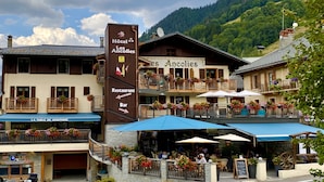 A hotel with a restaurant and bar, outdoor seating with umbrellas, and a mountainous backdrop. - Hotel Les Ancolies (Beaufort)