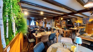 A restaurant interior with wooden tables, chairs, and a green wall with plants. - Hotel Les Ancolies (Beaufort)