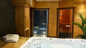 A wooden interior with a hot tub, a glass door leading to a sauna, and a brick wall. - Hotel Les Ancolies (Beaufort)