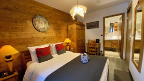 A bedroom with a wooden headboard, a bed with white and red pillows, a bedside lamp, and a nightstand. - Hotel Les Ancolies (Beaufort)