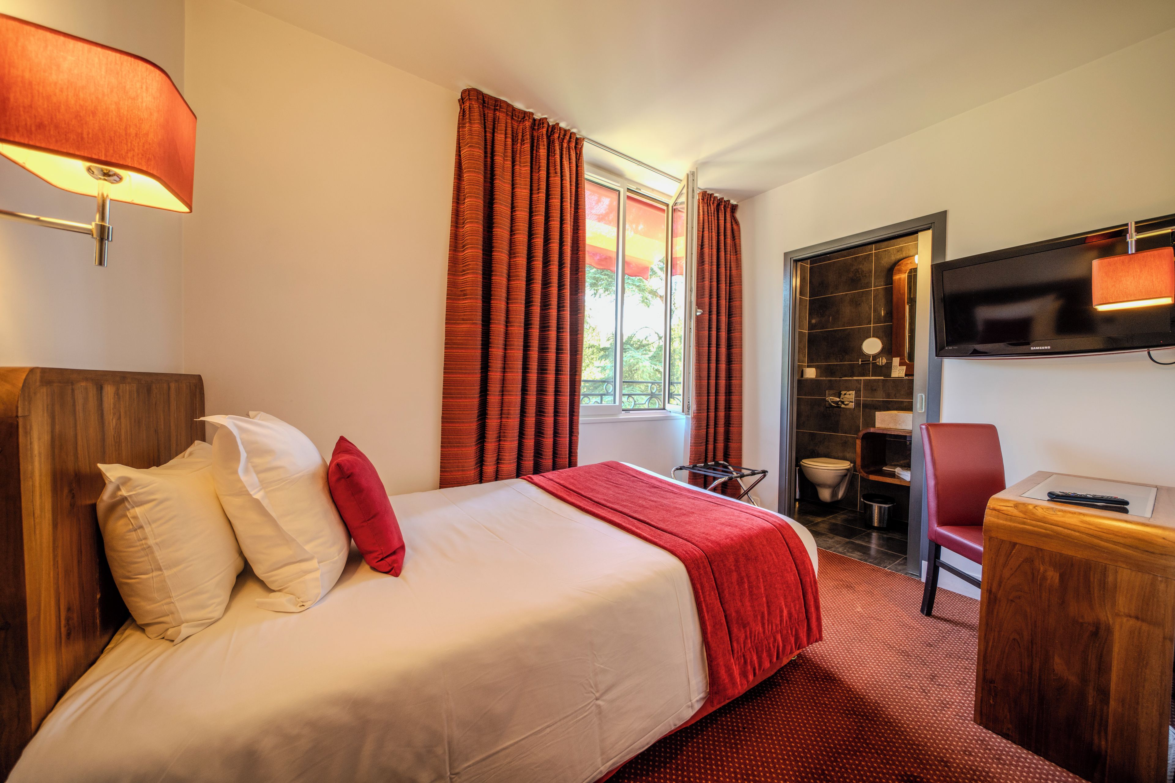 A hotel room with a bed, a desk, a TV, and a bathroom.