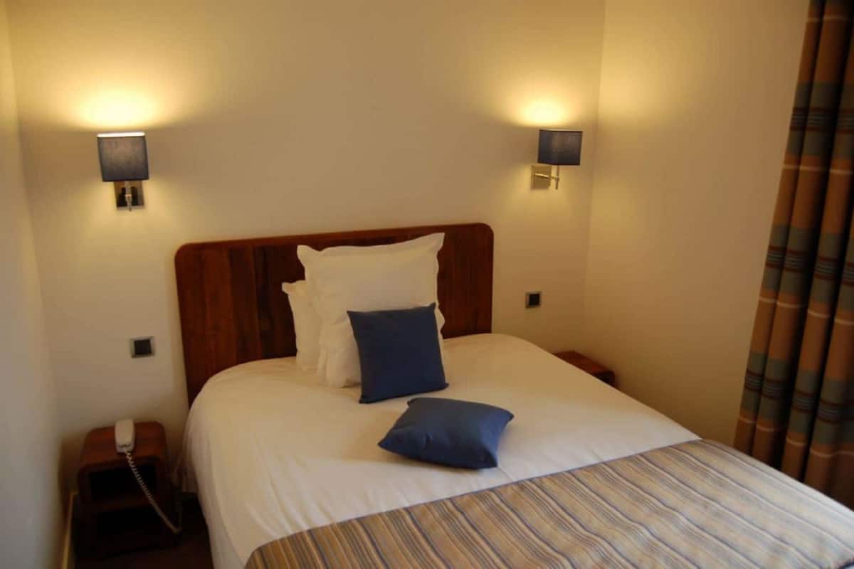 Quarto de hotel com uma cama grande, duas luminárias de cabeceira, um telefone e uma cortina.