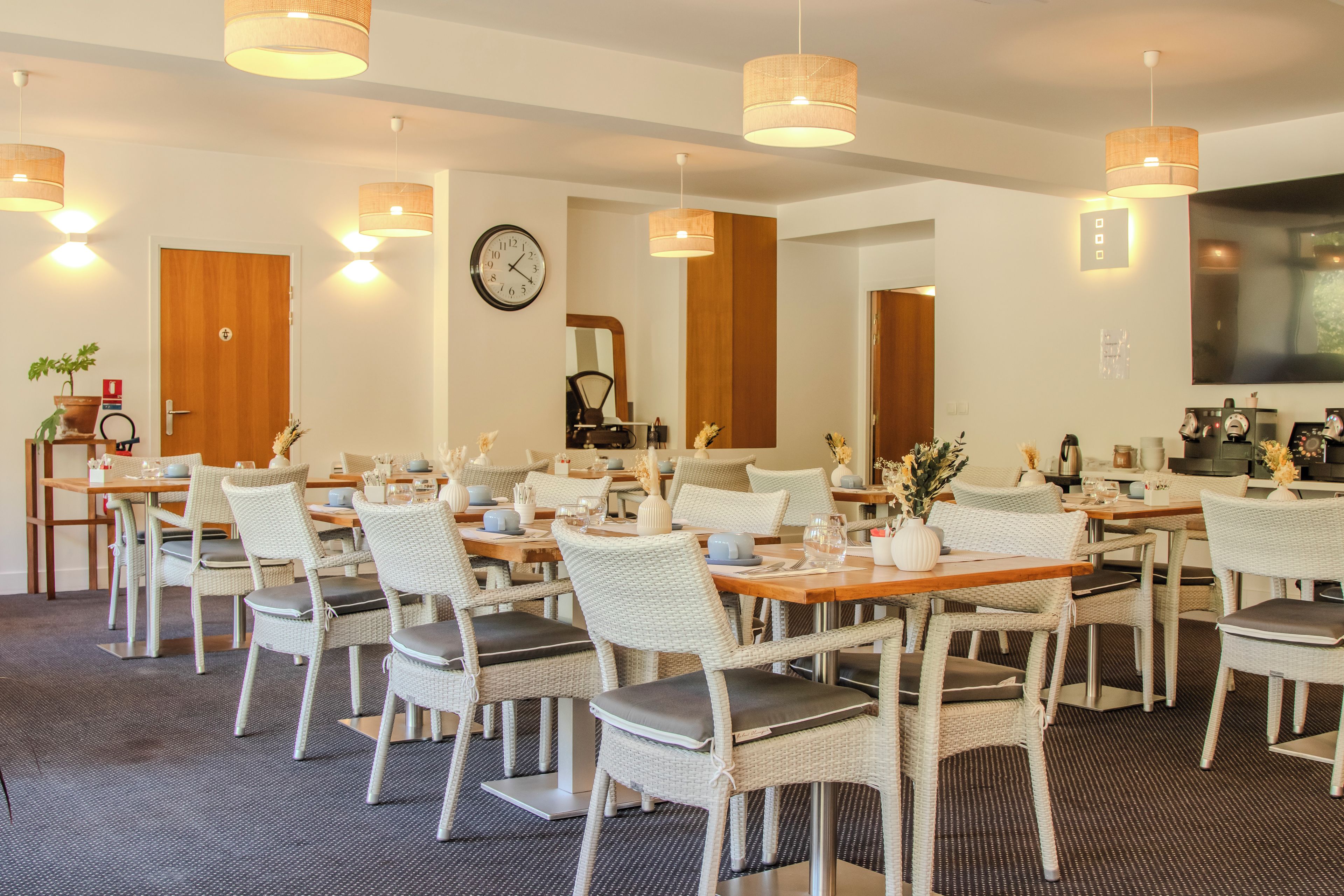 Un comedor de hotel con sillas de mimbre, mesas de madera e iluminación colgante.