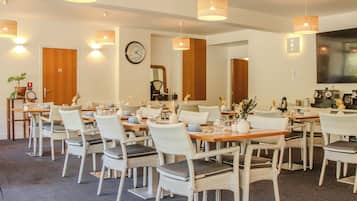 Un comedor de hotel con sillas de mimbre, mesas de madera e iluminación colgante.