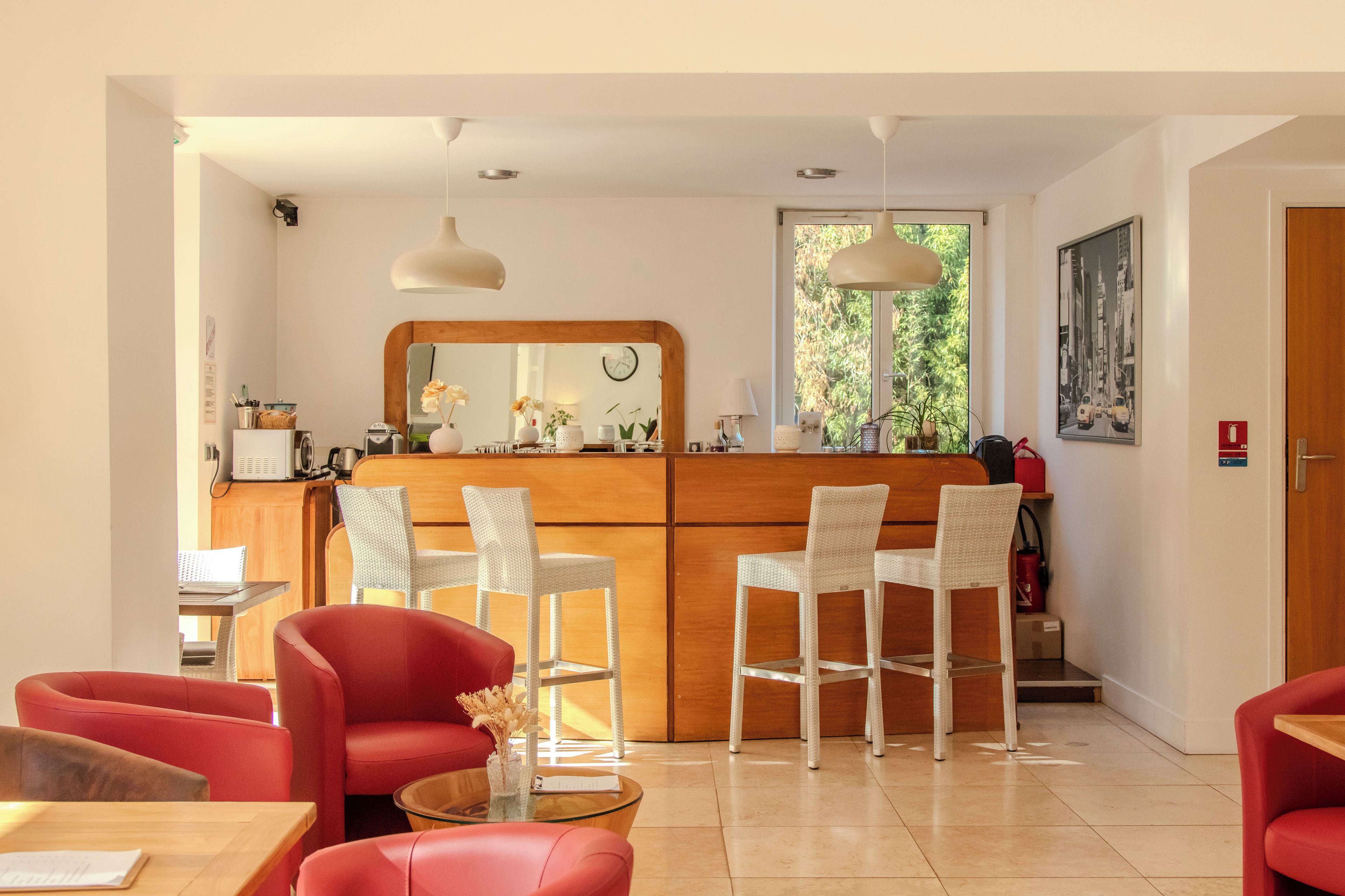 Cocina moderna con encimera de madera y sillas blancas, zona de comedor con sillas rojas y un amplio ventanal con follaje en el exterior.
