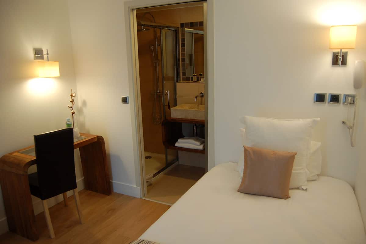 Quarto de hotel com cama, escrivaninha, cadeira, chuveiro e banheiro.
