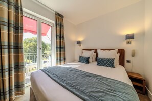 A bedroom with a bed, a nightstand, a wall-mounted phone, and a window with curtains.