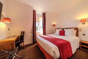 A hotel room with a bed, a desk, a chair, a nightstand, and a window with curtains. - Le Manoir De Sauvegrain (Saint-Lambert)