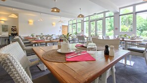 Un comedor con mesas dispuestas para dos personas, con sillas tejidas y una mesa de madera.