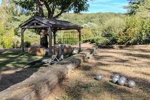 A gazebo with a bench, surrounded by a grassy area with a stone wall and metal balls. - Le Manoir De Sauvegrain (Saint-Lambert)