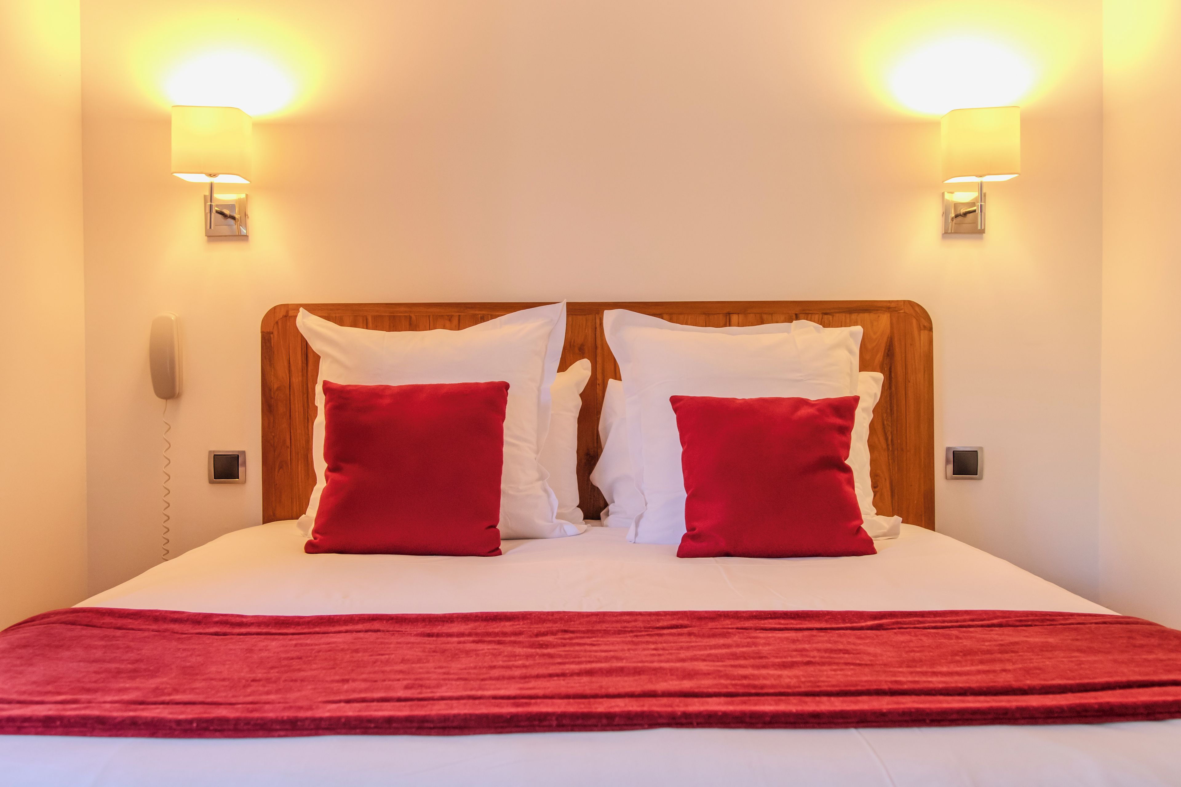 A bed with white bedding, two red pillows, and a wooden headboard.