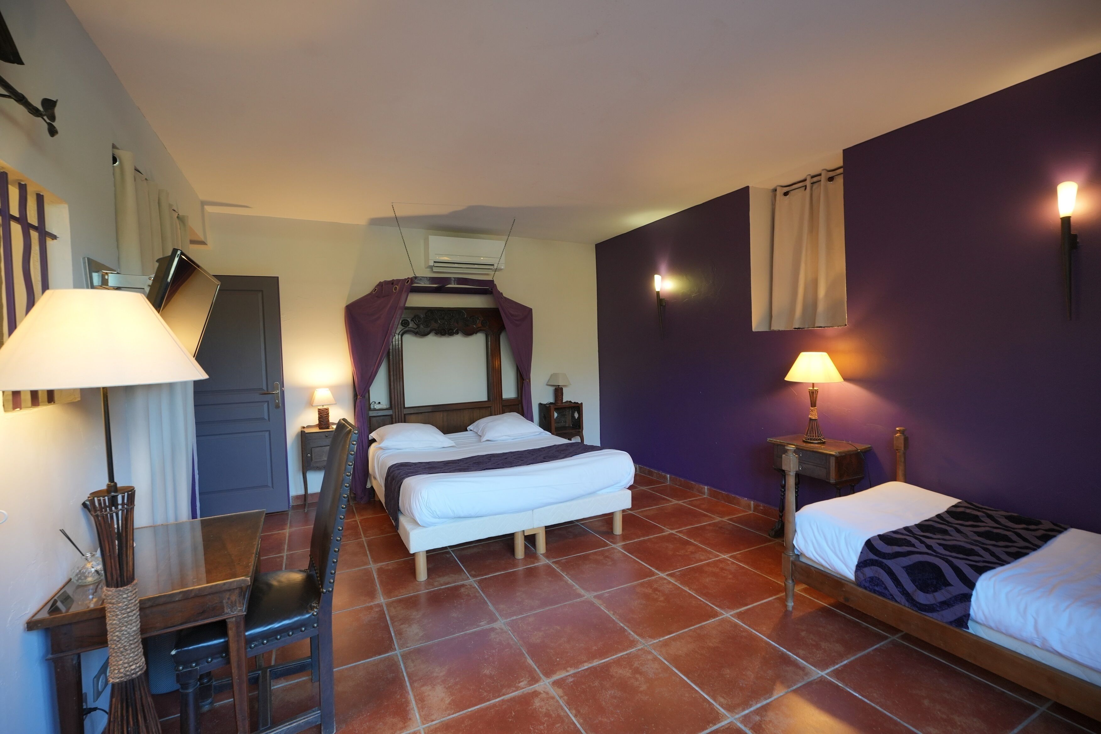 A bedroom with a bed, a desk, a chair, a nightstand, and a lamp.