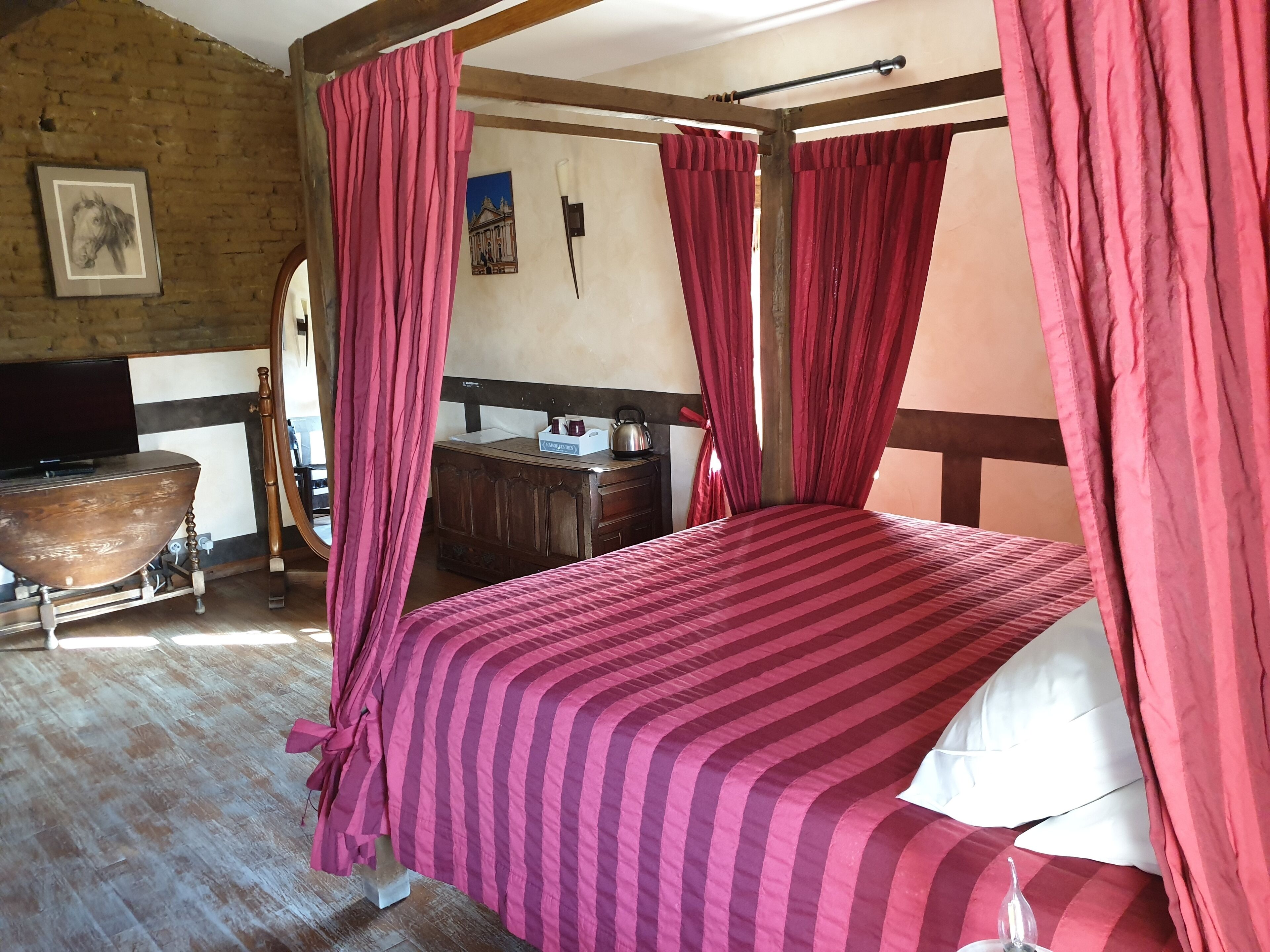Une pièce avec un lit, une commode en bois, un téléviseur et un tableau accroché au mur.