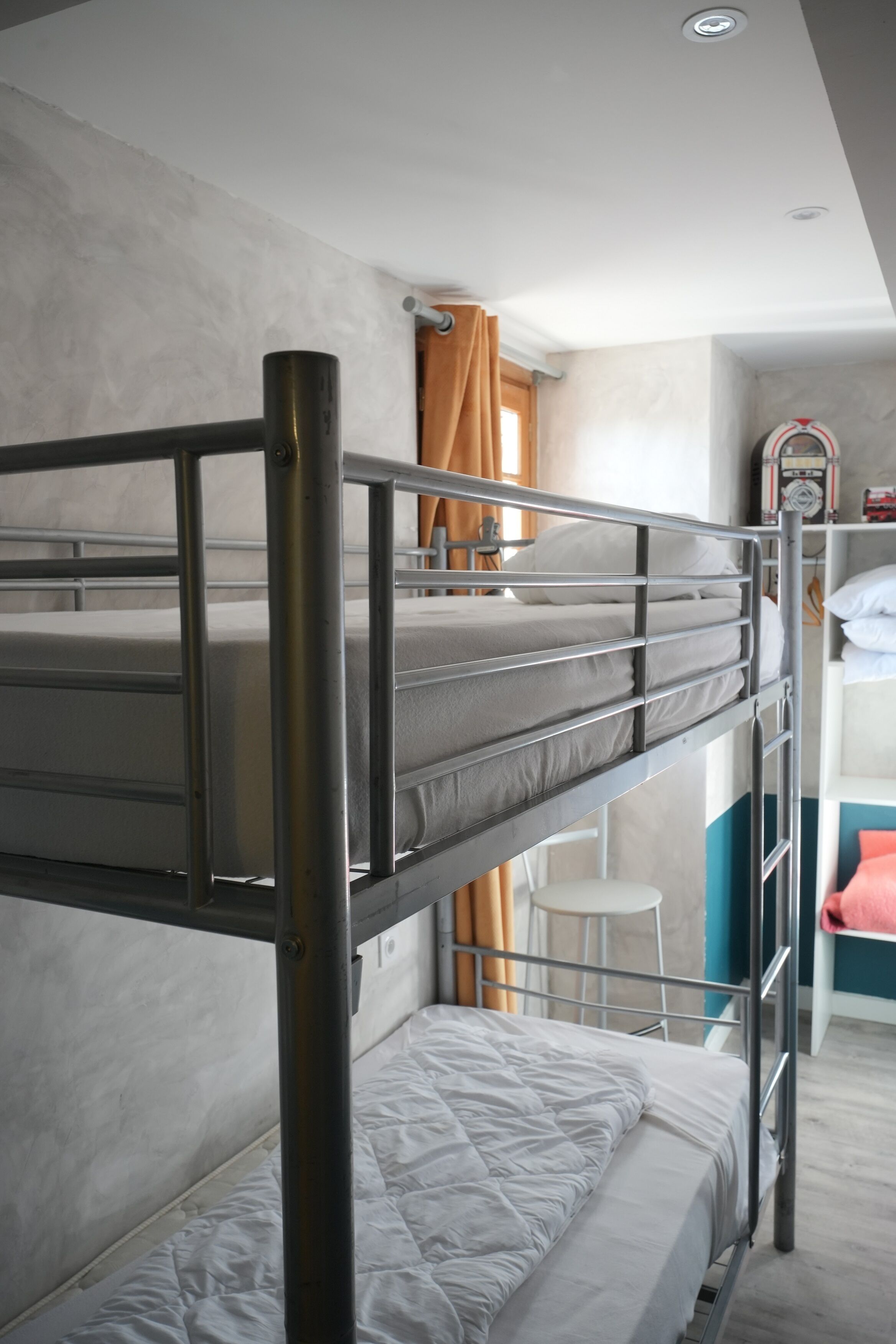 Ein Schlafraum mit Etagenbett, Metallgestell, weißer Matratze und kleinem weißen Stuhl.
