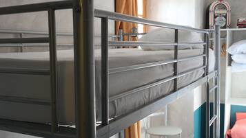 Ein Schlafraum mit Etagenbett, Metallgestell, weißer Matratze und kleinem weißen Stuhl.