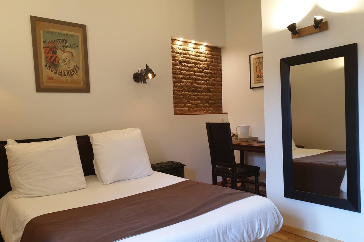 Ein Hotelzimmer mit Bett, Schreibtisch, Stuhl, großem Spiegel und Wandleuchte.