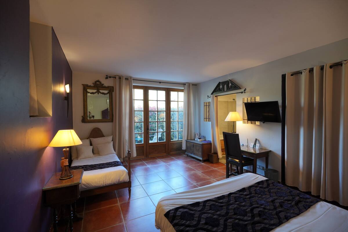 Ein Hotelzimmer mit zwei Betten, einem Schreibtisch, einem Stuhl, einem Fernseher und einem Fenster mit Vorhängen.