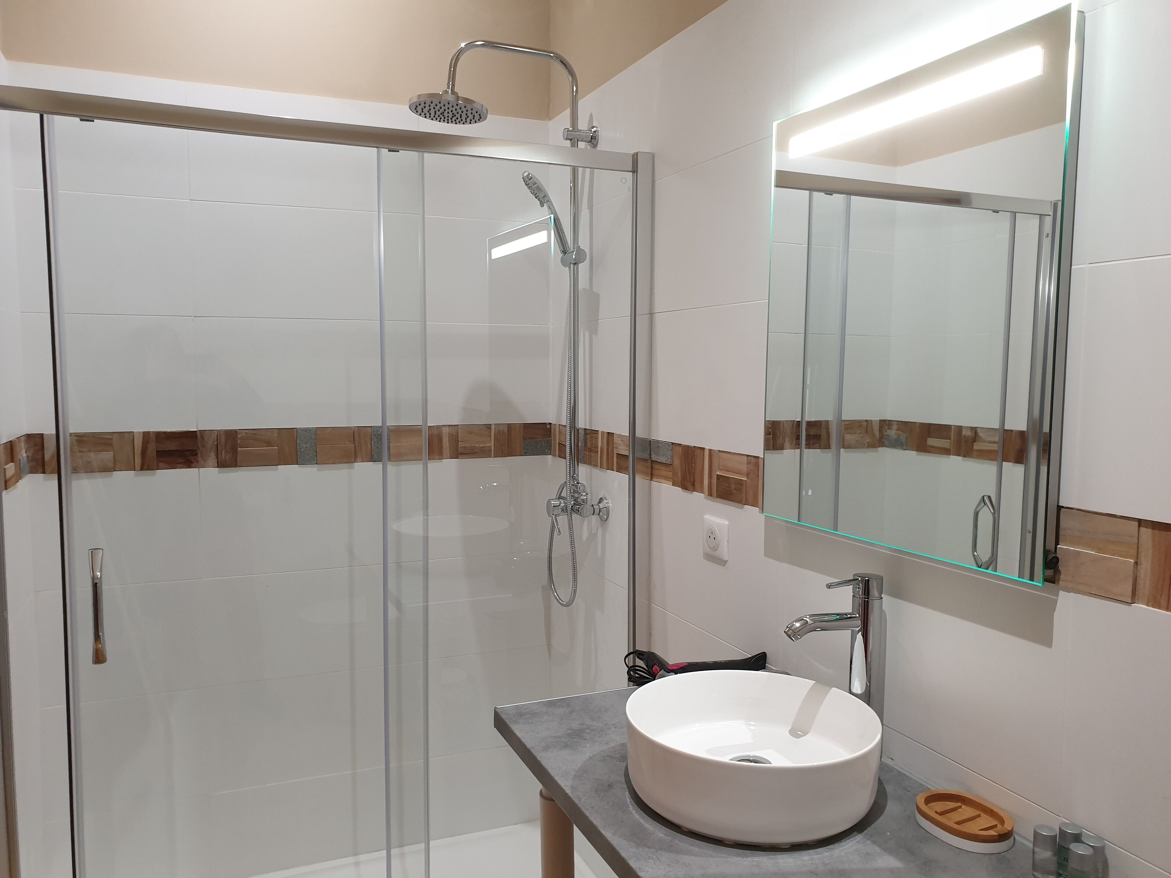 A modern bathroom with a glass-enclosed shower, a white sink with a wooden soap dish, and a mirror with a wooden frame.