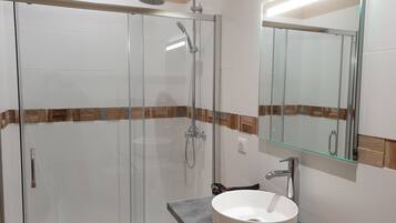 A modern bathroom with a glass-enclosed shower, a white sink with a wooden soap dish, and a mirror with a wooden frame.