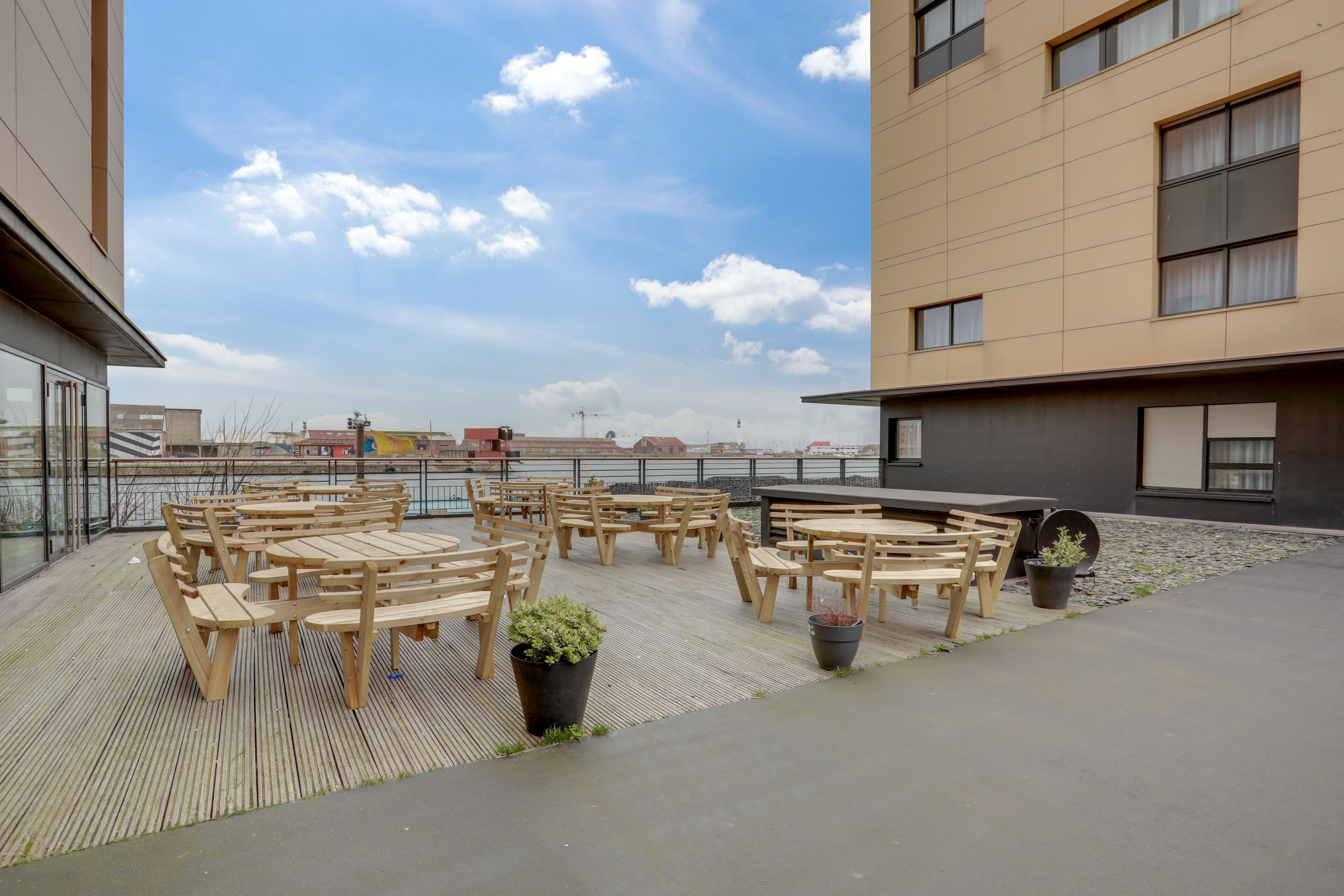 Une terrasse extérieure avec des tables et des chaises en bois, des plantes en pot et une vue sur le panorama urbain.