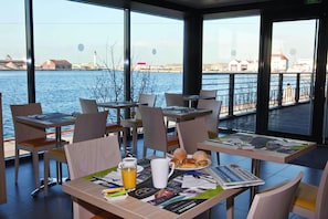 A dining area with tables set for breakfast, featuring croissants, a newspaper, and a glass of orange juice. - All Suites Appart Hôtel | Dunkerque Centre (Dunkirk)