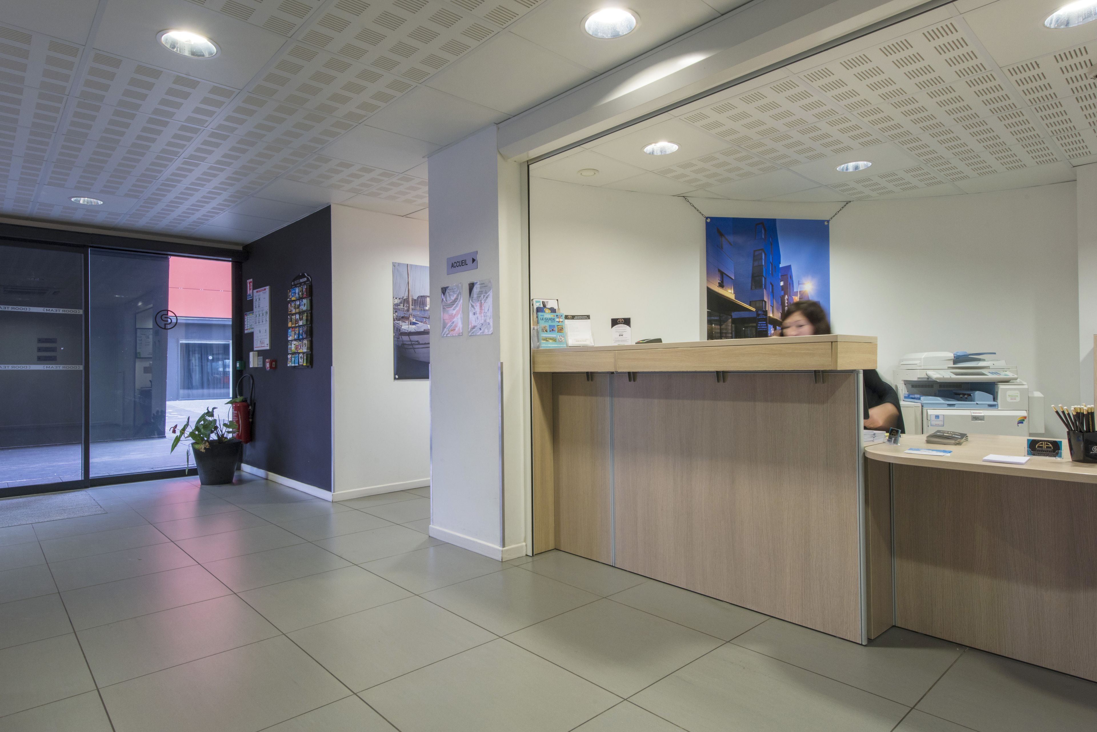 A reception area with a wooden counter, a fire extinguisher, and a potted plant.
