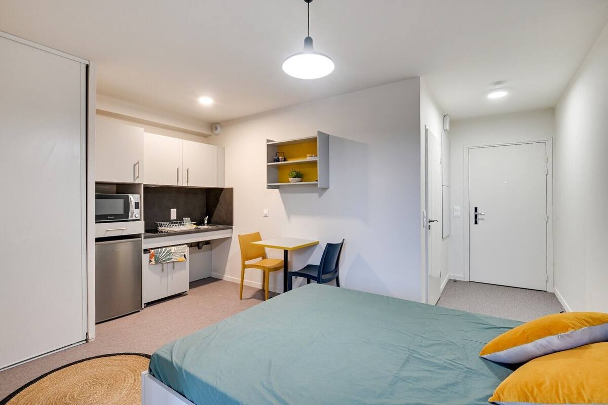 Une chambre compacte comprenant un lit, un bureau et une kitchenette.