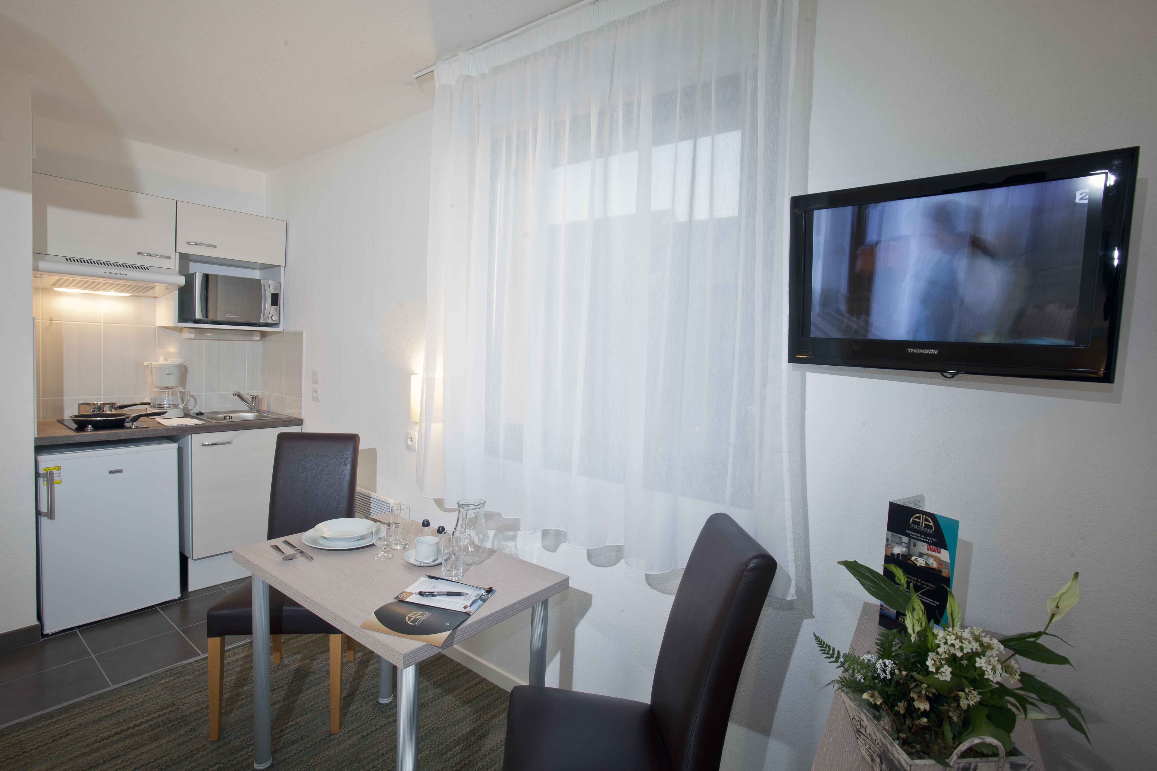 Ein Hotelzimmer mit Esstisch für zwei Personen, einer Mikrowelle, einem kleinen Kühlschrank und einem an der Wand montierten Fernseher.