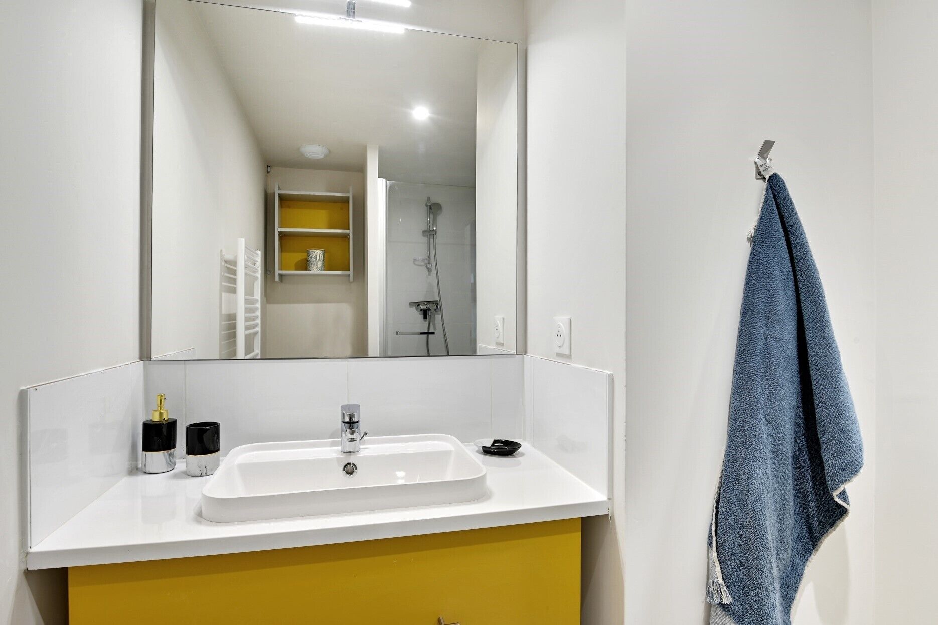A bathroom with a white sink, yellow cabinet, and a large mirror.