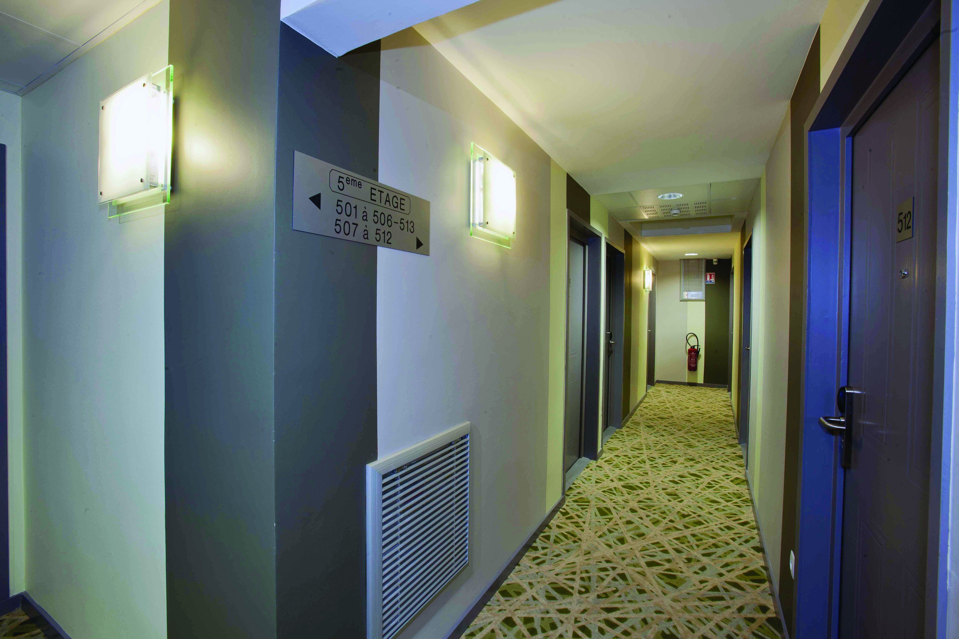 Un pasillo de hotel con carteles indicativos, un extintor y una alfombra estampada.