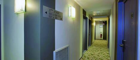 Un pasillo de hotel con carteles indicativos, un extintor y una alfombra estampada.