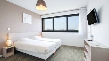 Hotelkamer met twee bedden, een bureau, een televisie, een raam met uitzicht en een lamp.