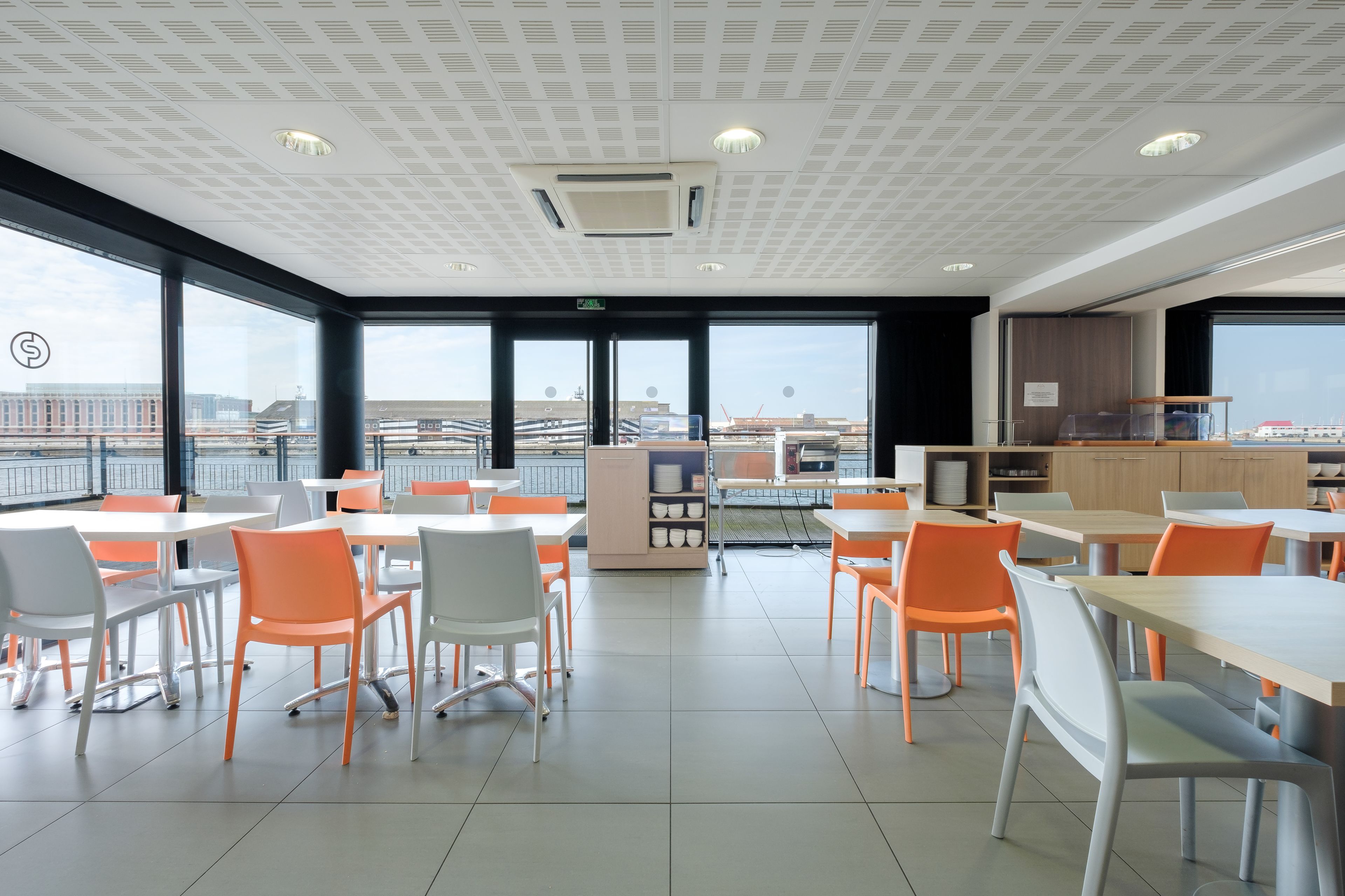 A modern dining area with tables and chairs, large windows, and a view of the cityscape.
