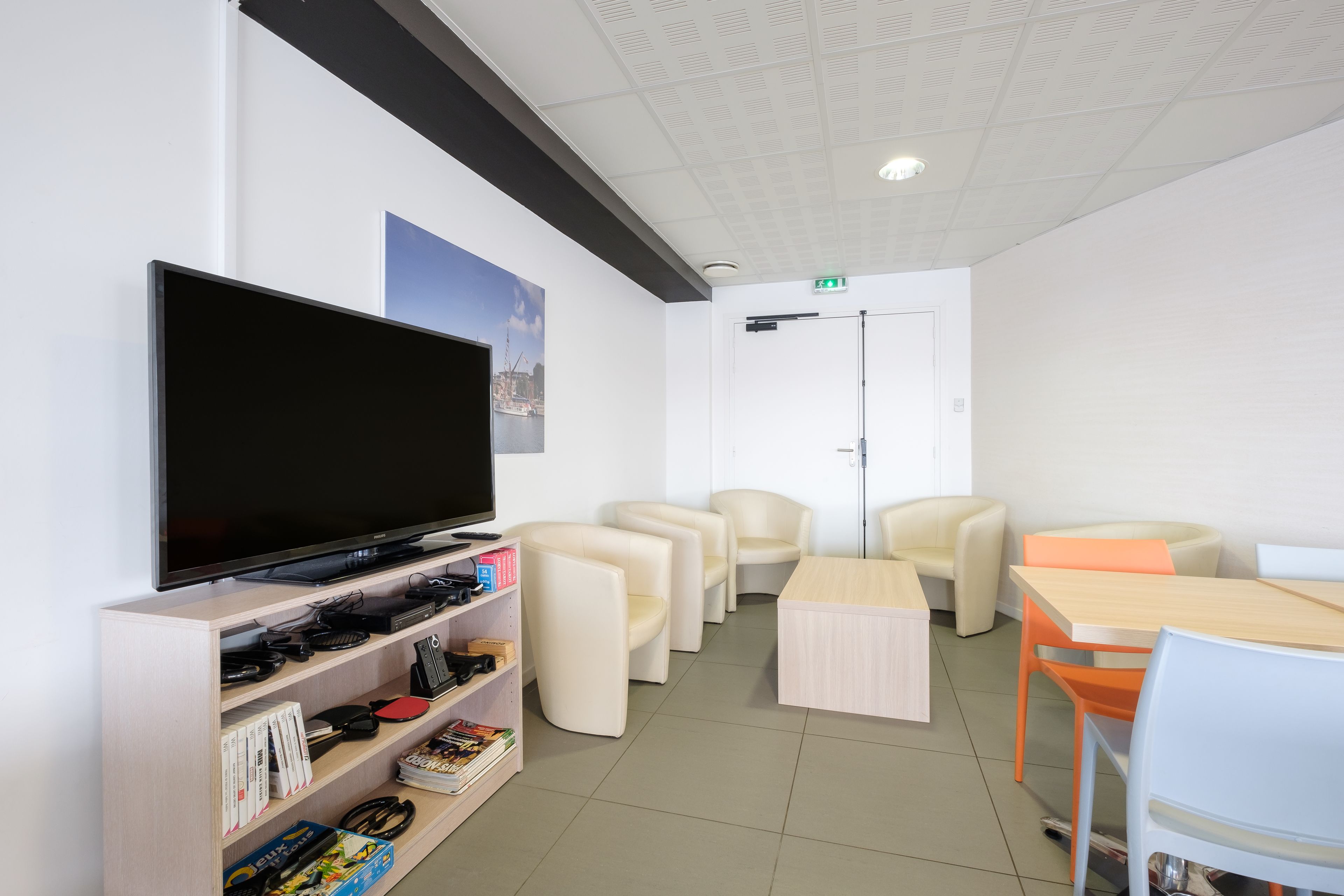 A modern room with a flat-screen TV, comfortable seating, a wooden table, and a bookshelf with various items.